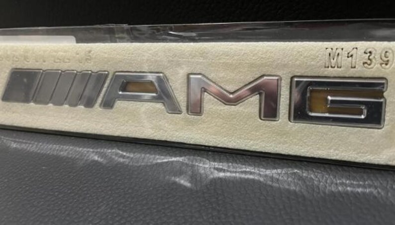 a close-up view of a silver and gold Mercedes-Benz logo on a beige background.
