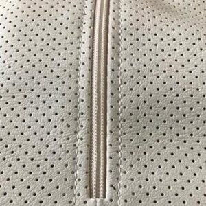 a close-up view of a white fabric with a perforated pattern, featuring a zipper running vertically down the center.