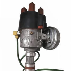 Könnte beinhalten: Ein Oldtimer-Verteiler mit schwarzer Kappe, braunen Anschlüssen und silbernem Gehäuse. Er hat ein grünes Kabel und einen gelben Stecker. Das Gerät hat eine kreisförmige Komponente an der Seite, vor weißem Hintergrund.