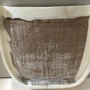 a white object with a textured surface, possibly a piece of furniture or a decorative item. The object appears to be made of a material that resembles burlap or burlap-like fabric, with a white base or frame. The object is placed against a plain white background, which highlights its details and textures.