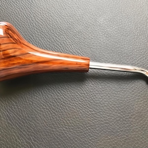 May include: A wooden pipe with a polished, glossy finish. The pipe's bowl is a warm brown with visible wood grain, transitioning to a silver metal stem. The stem curves slightly and ends with a textured tip.
