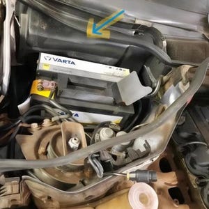the engine compartment of a car, with various components and parts visible, including a battery and other mechanical parts.