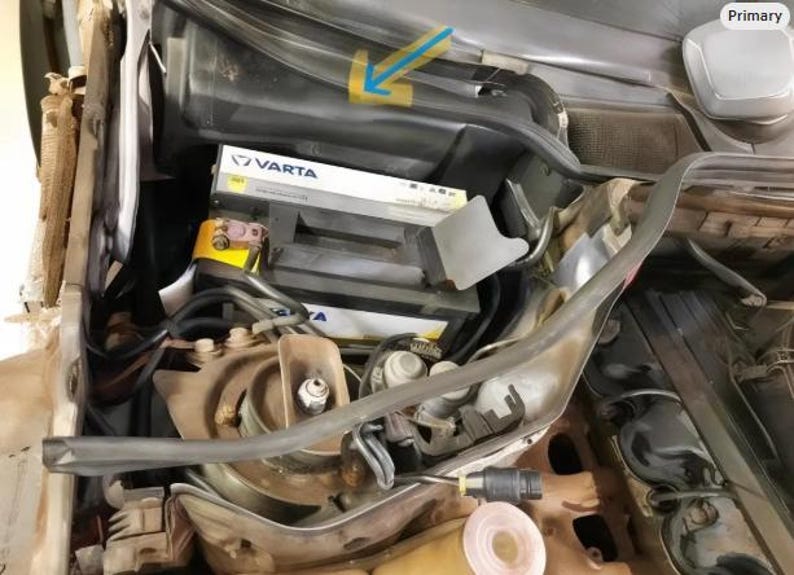 the engine compartment of a car, with various components and parts visible, including a battery and other mechanical parts.