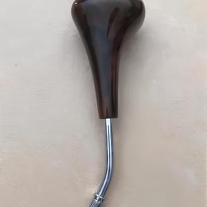 May include: A dark brown, teardrop-shaped gear shift knob with a polished finish. The knob is attached to a curved, chrome-colored metal rod. The bottom of the rod has a textured, silver-colored grip.
