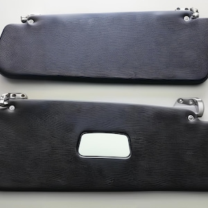 May include: Two black car sun visors with a textured finish and chrome mounting hardware. One visor has a rectangular mirror. The visors are displayed against a white background. Automotive accessories.