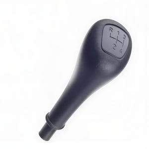 May include: A black gear shift knob with a textured surface. The top of the knob has an inset with a gear pattern showing the positions 1, 2, 3, 4, and reverse. The knob has a long, tapered handle.