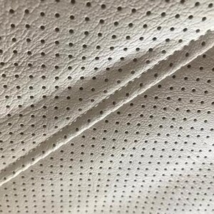 a close-up view of a white fabric with a perforated pattern, featuring numerous small holes or dots arranged in a grid-like pattern.