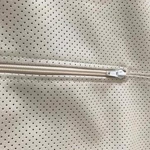 A close-up view of a zipper on a fabric with a perforated pattern.