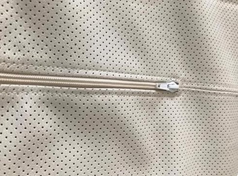 A close-up view of a zipper on a fabric with a perforated pattern.