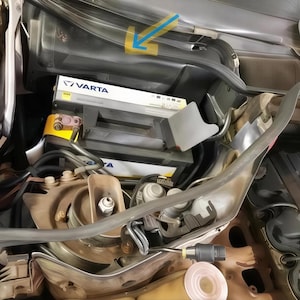 May include: An engine compartment with a VARTA battery, various wires, and mechanical components. The battery is black and gray, with the VARTA logo visible. The image is taken from an overhead angle, showing the complexity of the engine's internal workings.