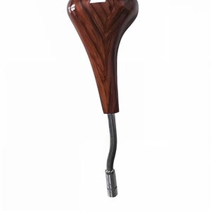 Può includere: Un pomello del cambio in legno con finitura lucida. Il pomello è di colore marrone scuro con un motivo a venature del legno. Il pomello del cambio ha un albero di metallo curvo e una base color argento.
