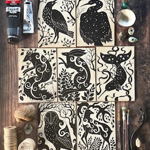 May include: Set of eight black and white illustrations featuring various animals and plants. The illustrations are printed on a cream-colored background and are framed with a black border. The animals include a fox, a rabbit, a bird, a deer, an owl, and a narwhal.