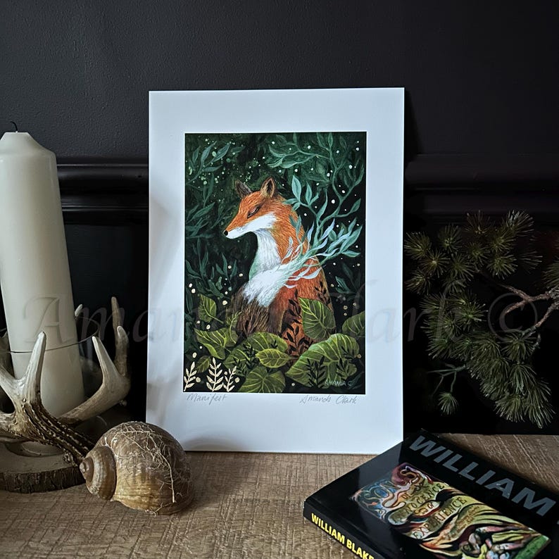 May include: A print of a fox sitting in a forest with green leaves and white flowers. The fox is orange and white with a black nose and black eyes. The print is titled "Manxfer" and signed "Amanda Clark".