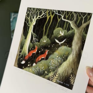 May include: A print of a dark forest scene with two red foxes walking through the woods. The forest is filled with trees, leaves, and glowing lights. The print is signed "Amanda Clark".