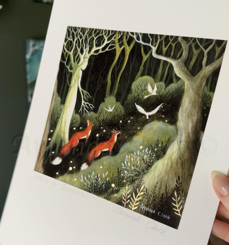 May include: A print of a dark forest scene with two red foxes walking through the woods. The forest is filled with trees, leaves, and glowing lights. The print is signed "Amanda Clark".