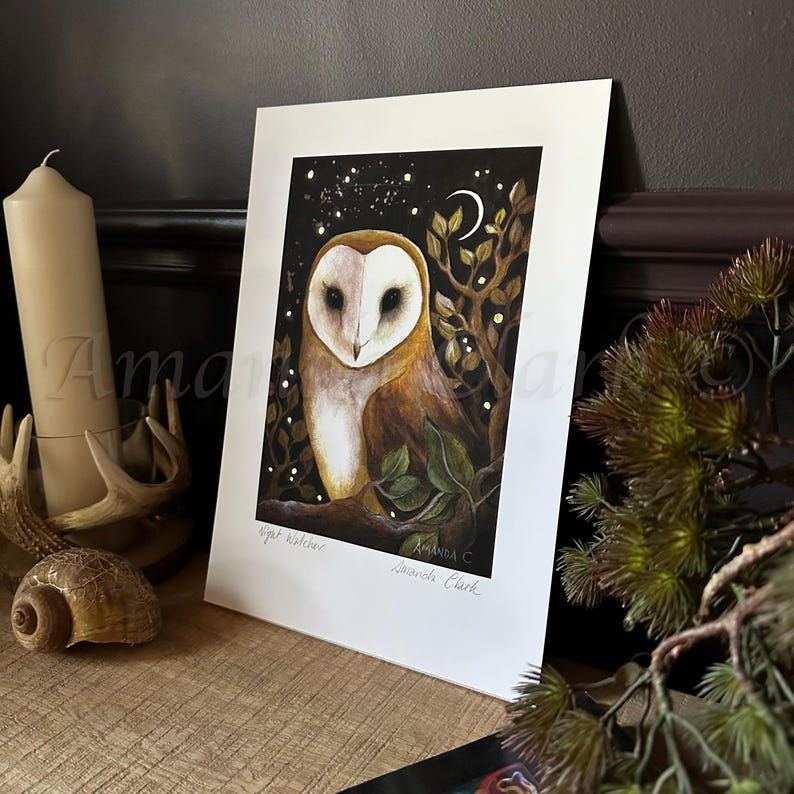 Puede incluir: Un b&uacute;ho de granero blanco y marr&oacute;n con ojos negros est&aacute; posado en una rama en un bosque oscuro. El b&uacute;ho est&aacute; mirando directamente al espectador. El fondo es un bosque oscuro con una luna creciente y estrellas. El texto "Night Watcher" y "Amanda C.  Edwards Clark" est&aacute; impreso debajo del b&uacute;ho.