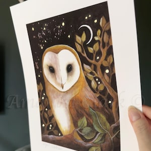 Puede incluir: Un b&uacute;ho blanco y marr&oacute;n con grandes ojos oscuros est&aacute; posado en una rama en un bosque oscuro. El b&uacute;ho est&aacute; rodeado de hojas doradas brillantes y una luna creciente. El fondo es azul oscuro con estrellas doradas.