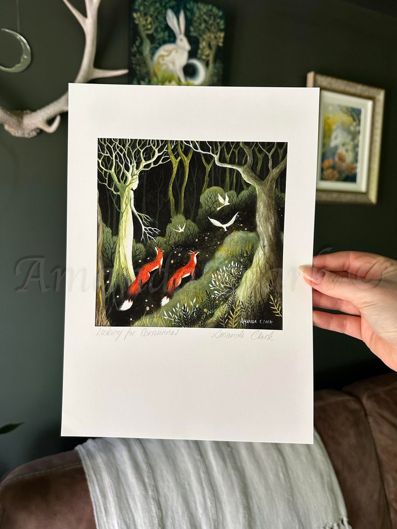 May include: A print of a painting depicting a forest scene with a white figure in the center, surrounded by trees and foliage. Two red foxes are walking towards the figure, and there are white birds flying in the air. The text "Listening for Corvus" and "Amanda Clark" is written at the bottom of the print.
