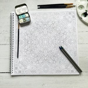 Puede incluir: Una p&aacute;gina de libro para colorear de mandala en blanco y negro con un dise&ntilde;o detallado. La p&aacute;gina est&aacute; abierta sobre una mesa blanca con un juego de acuarelas y l&aacute;pices.