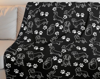 Puede incluir: Manta de tiro negra y blanca con un patrón repetido de perros salchicha y huellas de patas.
