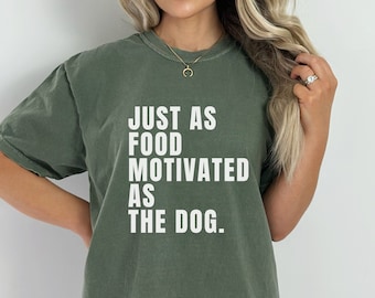 May include: A green t-shirt with the text "JUST AS FOOD MOTIVATED AS THE DOG." printed in white.