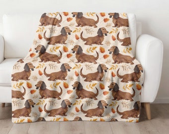 May include: A cream-colored throw blanket with a repeating pattern of brown dachshund dogs and orange and brown leaves.