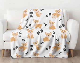 Könnte beinhalten: Weiße Fleece-Decke mit einem sich wiederholenden Muster aus braunen und weißen Corgis und schwarzen Pfotenabdrücken.