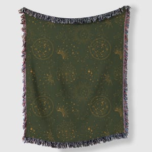 Puede incluir: Una manta tejida verde con un patrón celestial dorado. El patrón presenta estrellas, lunas y soles.