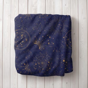 May include: A navy blue throw blanket with a gold celestial pattern. The pattern features stars, constellations, moons, and suns.