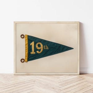 May include: A framed print of a vintage pennant with a dark green background and gold lettering. The pennant reads "19th".