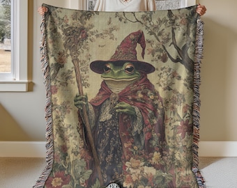 May include: A tapestry throw blanket featuring a green frog wearing a red and purple wizard hat and holding a staff. The frog is surrounded by flowers and foliage in a vintage style.