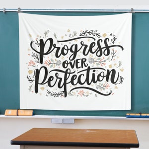 K&ouml;nnte beinhalten: Wei&szlig;e Wandbeh&auml;nge mit dem Text "Progress over Perfection" in schwarzer Schrift. Der Text ist von einem floralen Design in Rosa-, Blau- und Gelbt&ouml;nen umgeben.