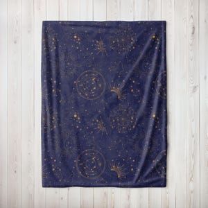 May include: A navy blue fleece throw blanket with a gold constellation pattern. The pattern features stars, moons, and sun symbols.