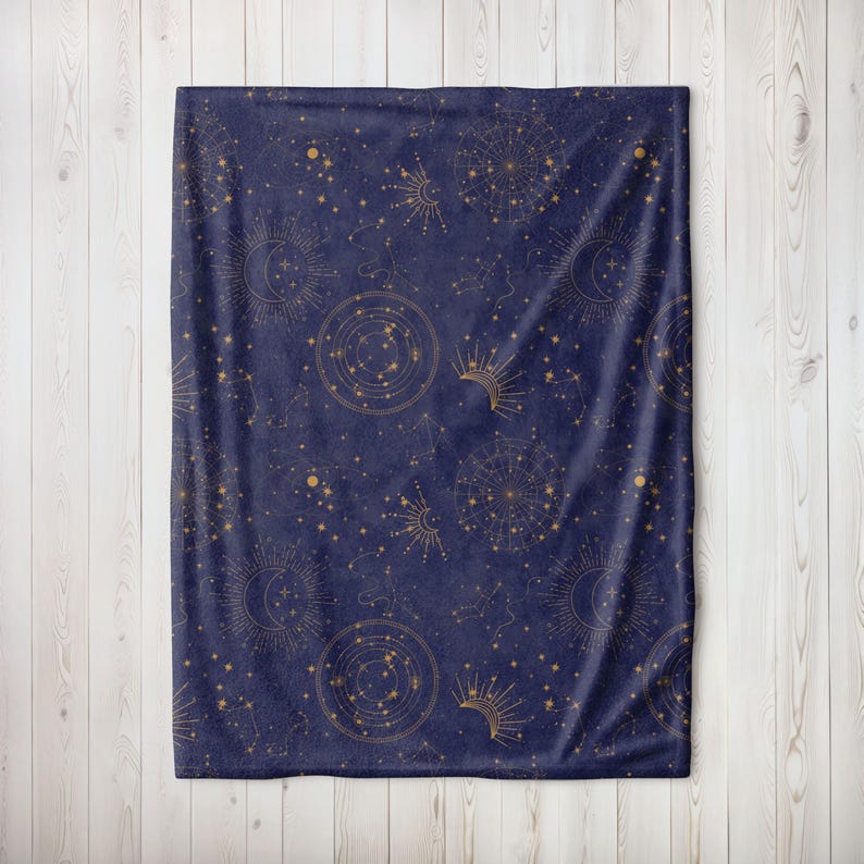 May include: A navy blue fleece throw blanket with a gold constellation pattern. The pattern features stars, moons, and sun symbols.
