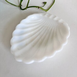 Può includere: Un piatto in vetro opalino bianco a forma di conchiglia di capasanta con bordo smerlato e creste radianti. Il piatto ha una finitura liscia e lucida e un centro concavo, progettato con una classica silhouette a forma di conchiglia.