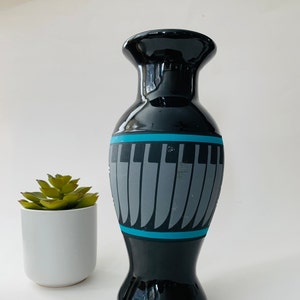May include: A black ceramic vase with a glossy finish. The vase features a teal band and a design of gray piano keys. The vase is next to a small potted succulent.