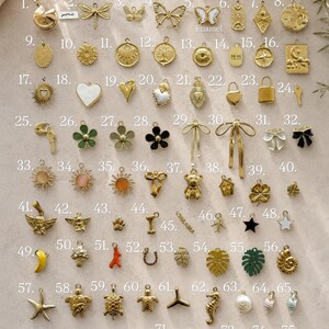 May include: A collection of seventy-five gold-toned metal charms arranged in a grid, featuring various shapes including butterflies, flowers, celestial symbols, animals, food items, and geometric designs, some with enamel accents and numbered labels.