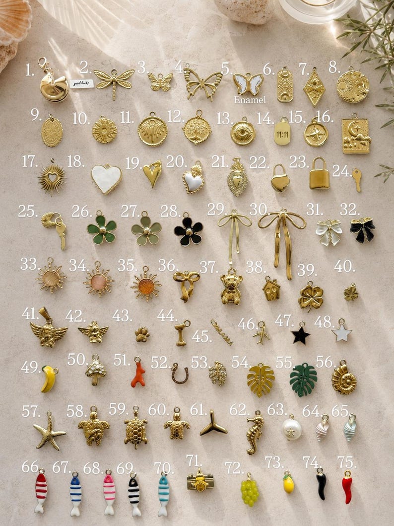 May include: A collection of seventy-five gold-toned metal charms arranged in a grid, featuring various shapes including butterflies, flowers, celestial symbols, animals, food items, and geometric designs, some with enamel accents and numbered labels.