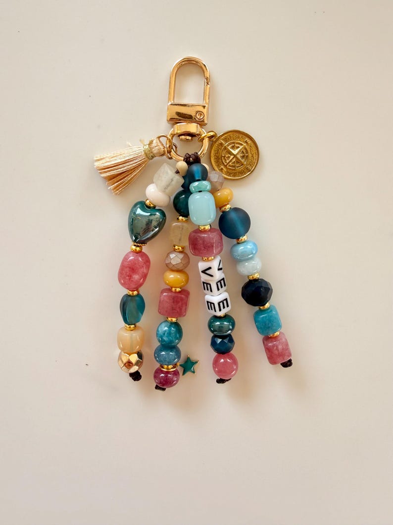 May include: A beaded keychain with a gold-colored clasp, tassel, and charm. The keychain features strands of colorful beads in shades of pink, blue, green, and gold. The word "LOVE" is spelled out in white letter beads.