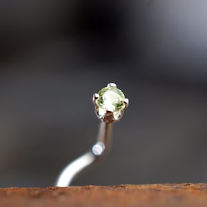 May include: A silver nose ring with a small, light green gemstone.