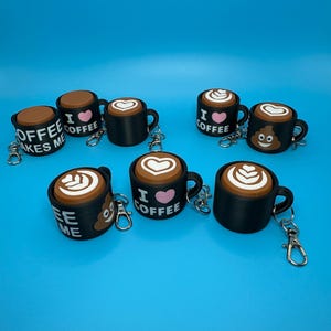 May include: A collection of black coffee mug keychains with various designs. Some mugs have the text "I ️ Coffee", while others feature latte art or a smiling poop emoji. Each keychain has a silver clasp.