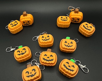 May include: A collection of orange pumpkin-shaped keychains with black carved faces and brown or green stems. Each keychain has a silver clasp. The keychains are arranged on a black surface, perfect for Halloween.