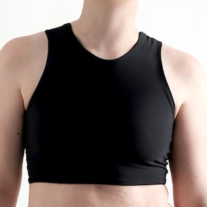 May include: A person with short, blue hair wearing a black crop top and black pants. They have a tattoo of a measuring tape on their left arm.