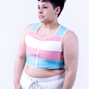 May include: A sleeveless cropped zip-up top featuring horizontal stripes in light blue, pink, and white. Paired with white drawstring shorts that have a matching light blue and pink striped waistband and a graphic print of raised fists at the hem.