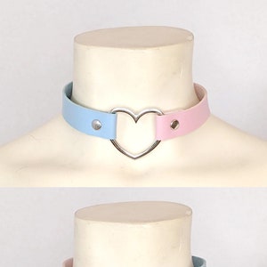Op de afbeelding: Een lichtblauwe en roze choker van imitatieleer met een zilveren hartbedel. De choker heeft twee drukknopen.