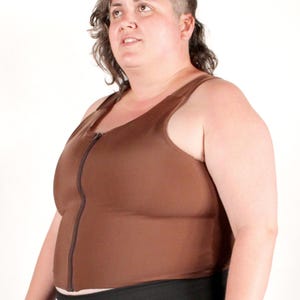 May include: A brown sleeveless compression top featuring a full-length front zipper closure. The garment is constructed from a smooth, solid-colored fabric and is worn with black athletic shorts that have a drawstring waist with silver metal aglets.