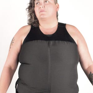 May include: A black compression tank top featuring a sleeveless design with a high neckline and a full-length vertical front zipper closure. The garment is constructed from a solid black fabric with a smooth texture and a fitted silhouette.