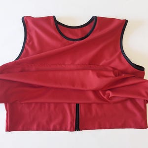May include: A red sleeveless vest with a black zipper and black trim around the neckline and armholes.