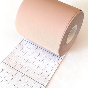 K&ouml;nnte beinhalten: Eine Rolle beigefarbene Stoffband mit einem Gittermuster auf dem Tr&auml;gerpapier. Das Band ist teilweise abgewickelt und zeigt die Klebeseite.