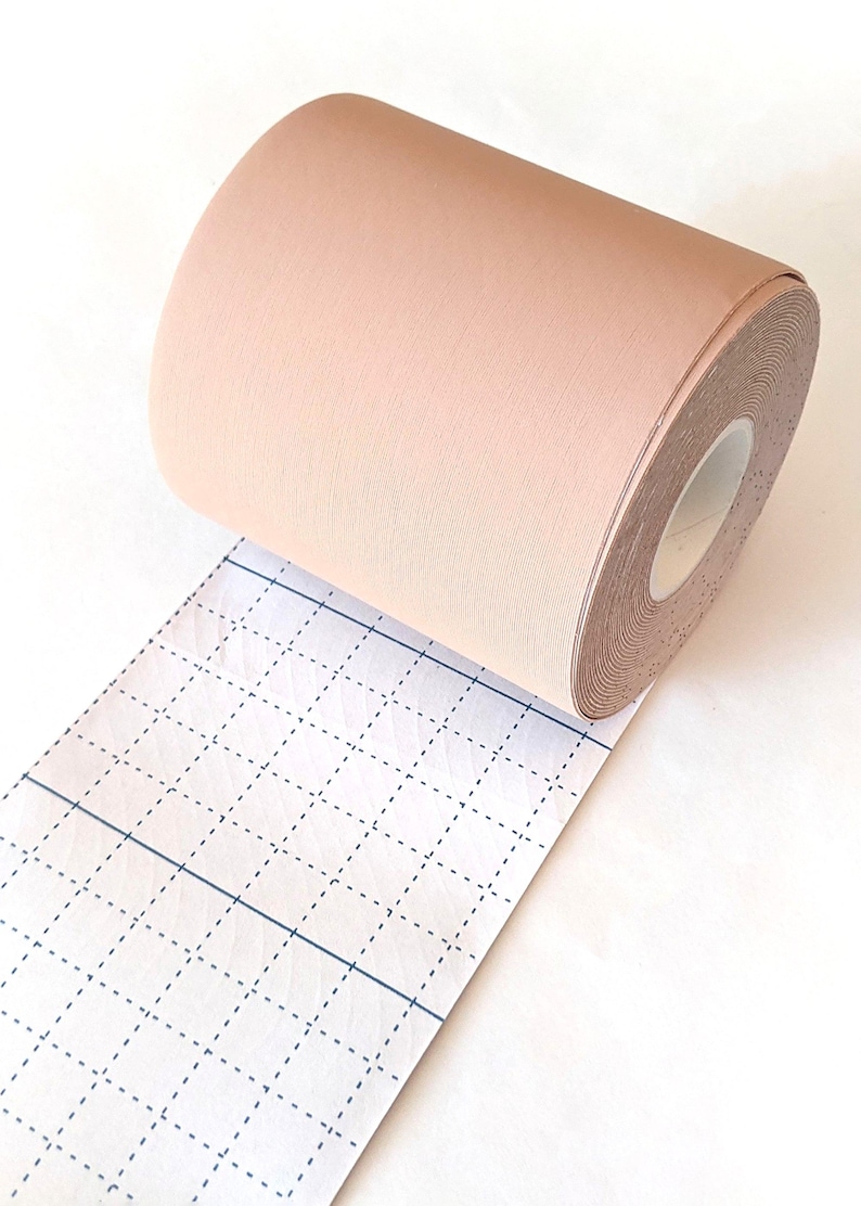 K&ouml;nnte beinhalten: Eine Rolle beigefarbene Stoffband mit einem Gittermuster auf dem Tr&auml;gerpapier. Das Band ist teilweise abgewickelt und zeigt die Klebeseite.